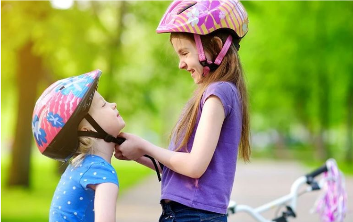 Decorative Picture of two girls with one fitting the other's bike helmet by Canva